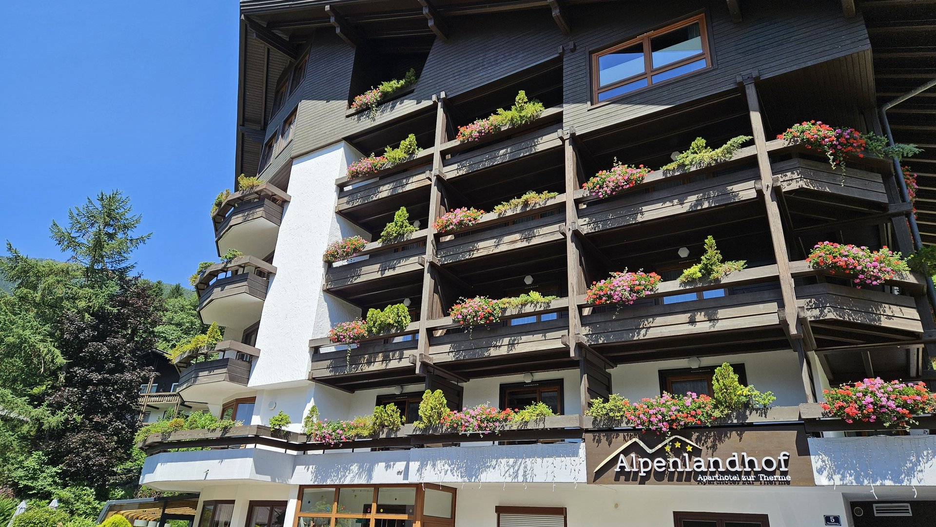 Traditionelles Hotel mit blumengeschmückten Balkonen und Holzdetails unter blauem Himmel.